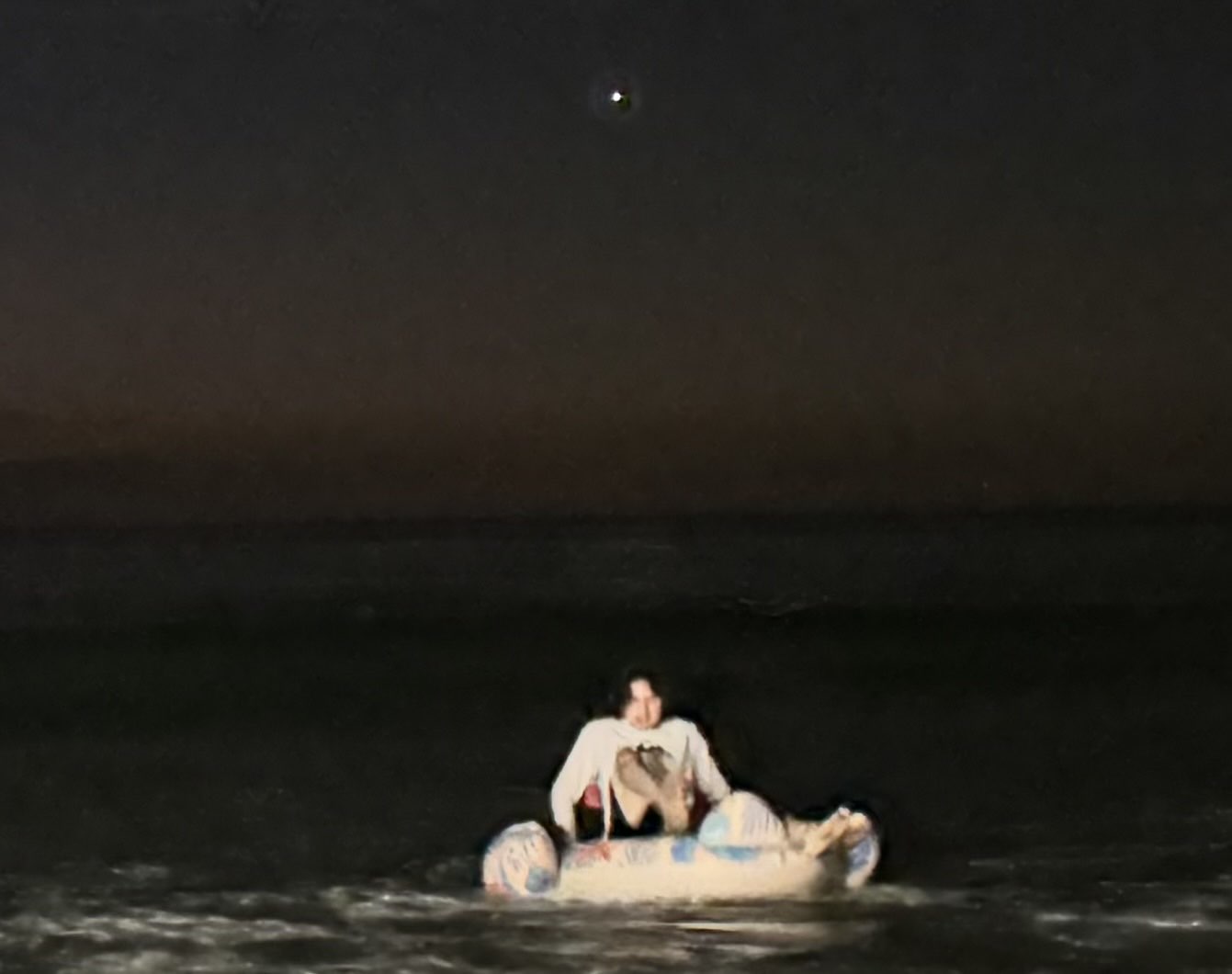 A person drifting in the ocean on an inflatable device at night