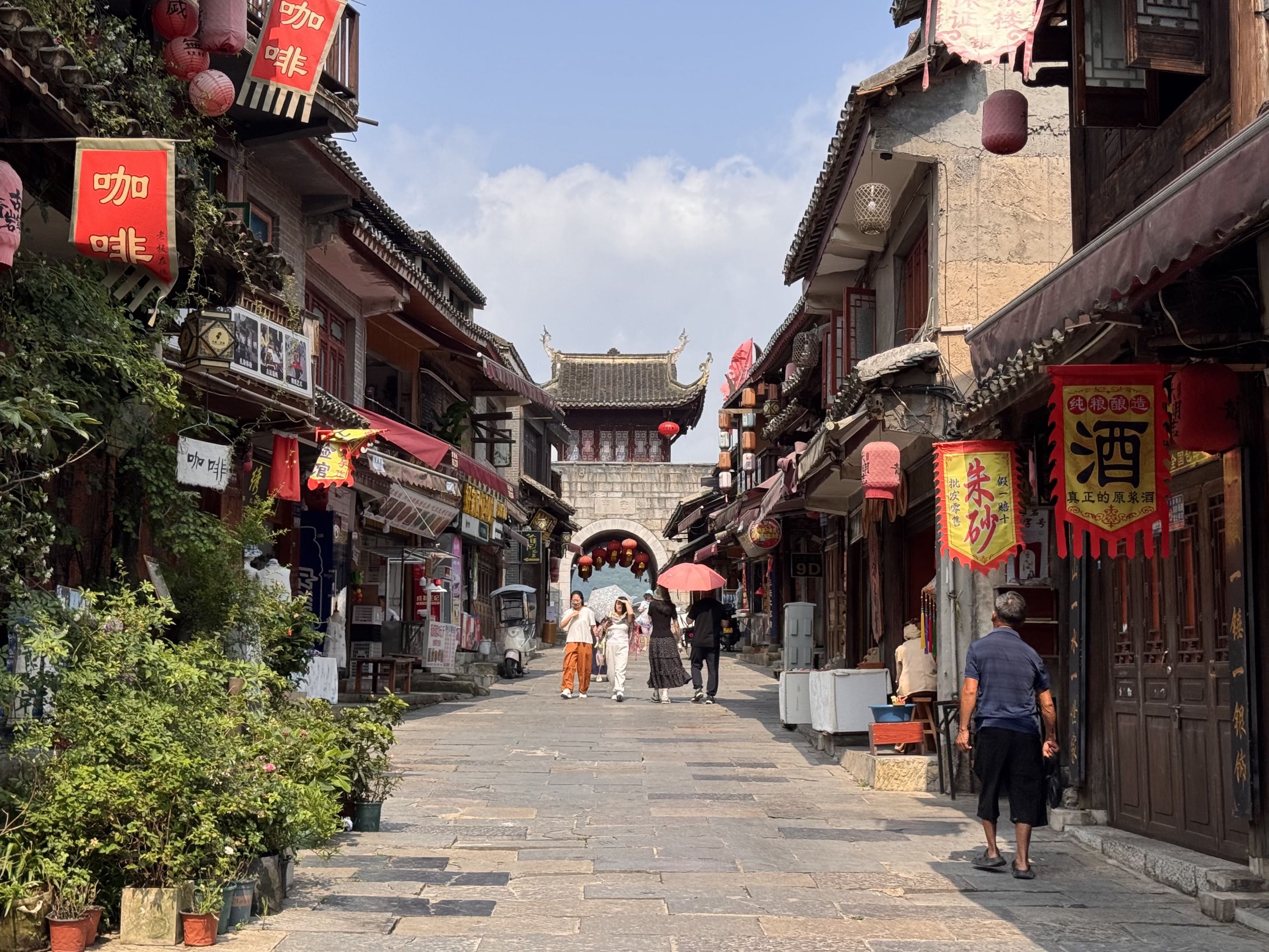 A sunlit old-town street lined with shops and hanging signs