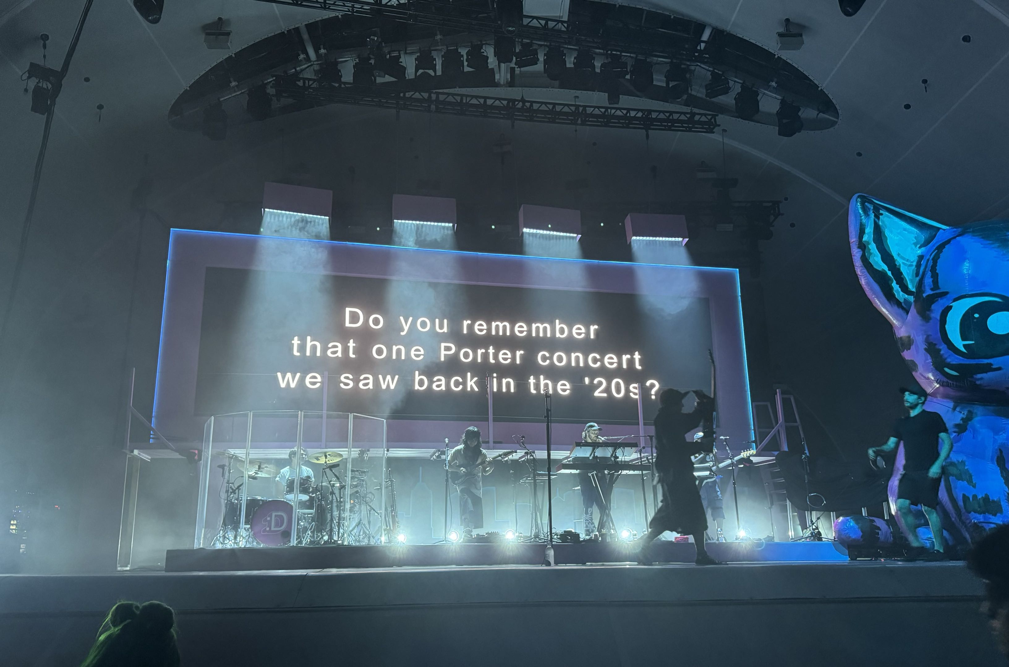A concert stage illuminated in blue light with text projected behind the performers